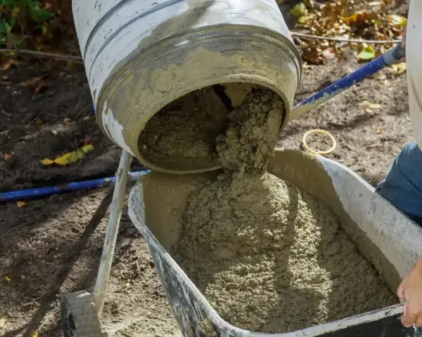 Betoniarka wylewa świeży beton do taczki. Widać, ile żwiru na metr sześcienny betonu jest w tej mieszance.