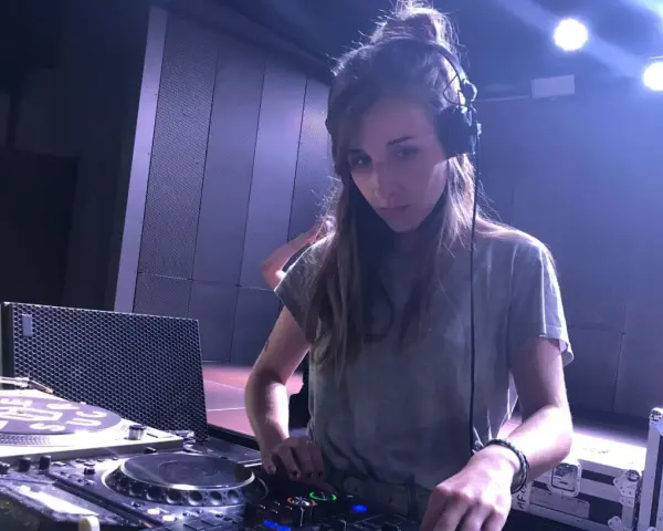 Une dj fille concentrée aux platines, casque sur les oreilles, dans une ambiance tamisée avec des lumières bleues.