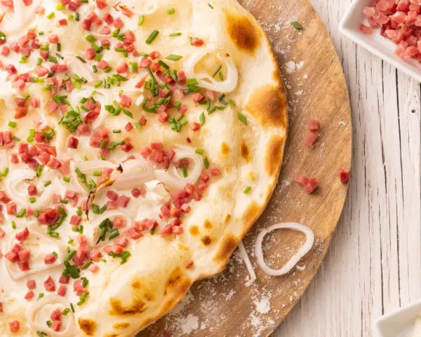 Flammkuchen vegetarisch mit Speckwürfeln, Zwiebelringen und Schnittlauch. Ein Genuss für jeden Gaumen!