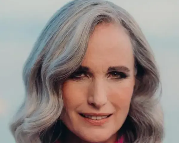 Mujer de 50 años con cabello plateado y ondulado, sonriendo suavemente. Se aprecian las líneas de expresión, reflejo de la flacidez facial a los 50.
