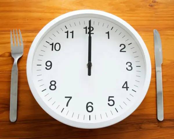 Uhr zeigt 12 Uhr. Gabel und Messer liegen bereit. Zeit für die Mittagspause während der Arbeitszeit.