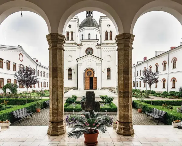 A courtyard with a cross and potted plants, framed by arches. The white church in the background is a place where monks like Father John and Brother Michael find peace.