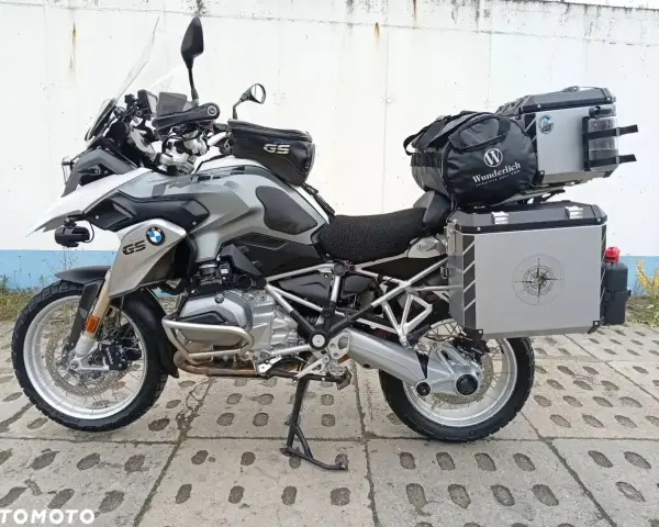 Srebrny motocykl BMW R1200GS z kuframi i torbą na bak. Wady tego modelu to m.in. wysoka cena i skomplikowana elektronika.