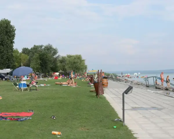 Ludzie odpoczywają na plaży i w wodzie. W tle widać kampery, co sugeruje, że to popularne miejsce na napfeny camping.