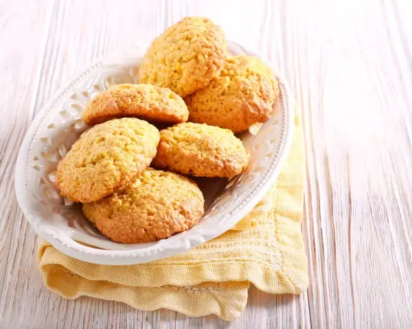 Biscotti con farina di mais dorati e friabili, serviti in un piatto bianco su un tovagliolo giallo.