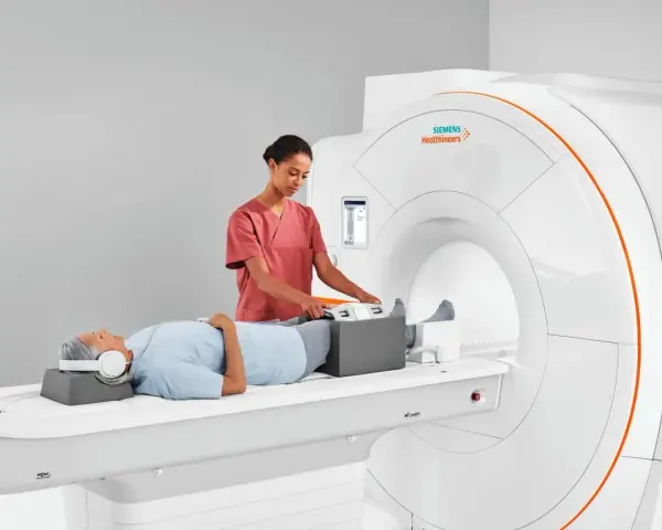 Pacjent leży na łóżku rezonansu magnetycznego, a technik przygotowuje jego nogi do badania. To właśnie mri co to za badanie, które pozwala zajrzeć do wnętrza ciała.