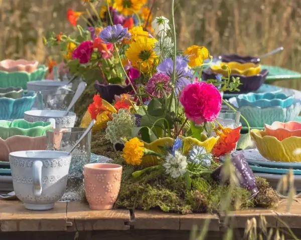Färgglada uppläggningsfat i plast, staplade med blommor och glas, skapar en festlig dukning utomhus.