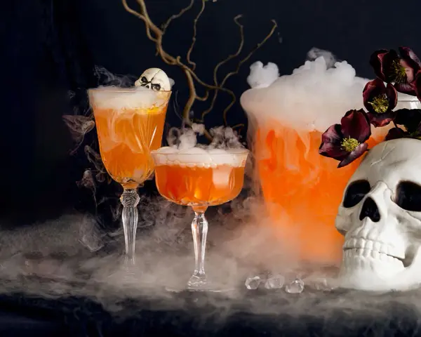 Två orangea drinkar med skum och en dödskalle, perfekt för en kuslig halloween-kväll.