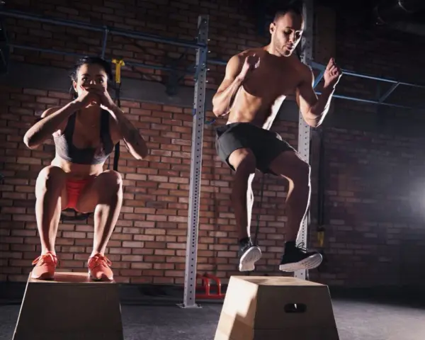 Para ćwicząca CrossFit wykonuje skoki na skrzyni w siłowni.