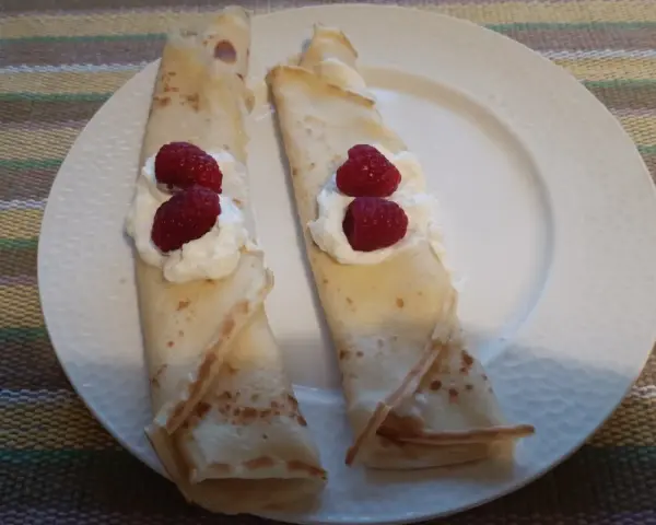 Dwa naleśniki z ricottą i malinami, ułożone na białym talerzu. Pyszny deser gotowy do zjedzenia.