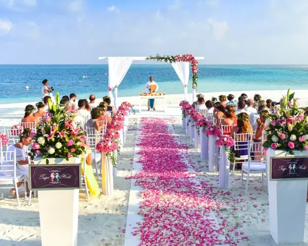 Piękna plażowa ceremonia ślubna. Kwiaty i płatki róż tworzą romantyczną ścieżkę. Goście siedzą na białych krzesłach, a ocean w tle.