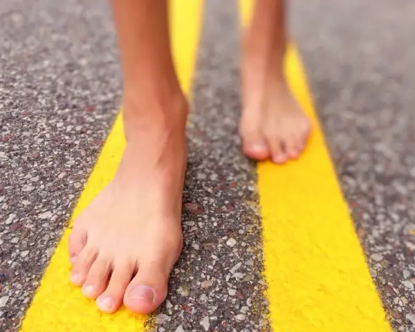 Piedi nudi che camminano su una strada con strisce gialle. Un'esperienza di correre scalzi per sentire la strada.