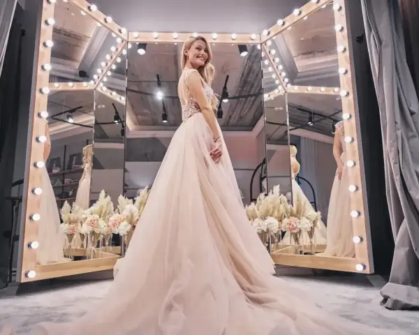 Uśmiechnięta panna młoda w tiulowej sukni przed lustrem. Zastanawiasz się, ile kosztuje wypożyczenie sukni ślubnej?