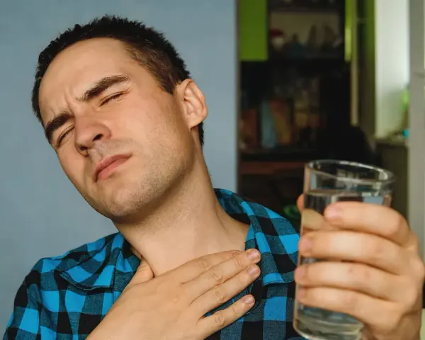 Mężczyzna z bólem gardła, cierpiący na nocny kaszel po alkoholu, sięga po szklankę wody.