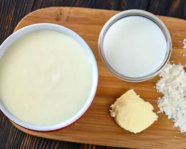 Zutaten für eine Mehlschwitze: Butter, Mehl, Milch und Salz auf einem Holzbrett.