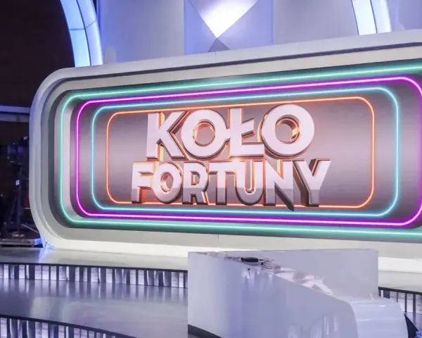 Na scenie studia telewizyjnego widnieje napis "KOŁO FORTUNY" otoczony neonami. To miejsce, gdzie marzenia o wygranej stają się rzeczywistością.