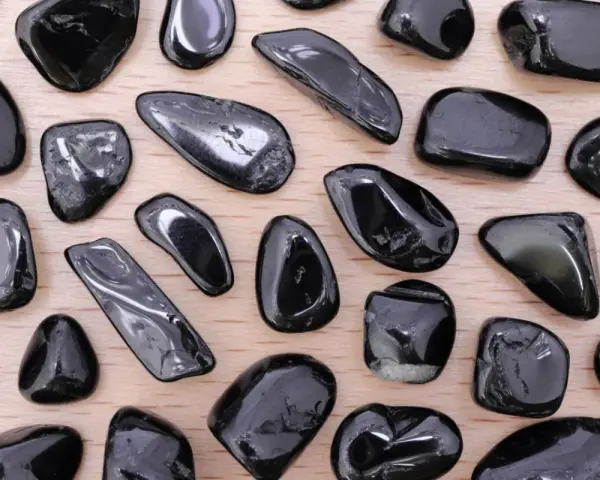 Tormalina nera, nota per le sue proprietà protettive e di radicamento, in una collezione di pietre levigate su fondo di legno.