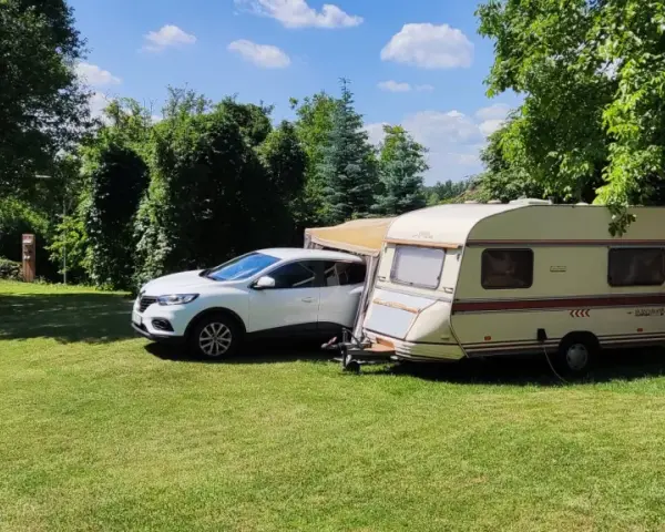 Biały samochód i przyczepa kempingowa na zielonej trawie, otoczone drzewami. Idealne miejsce na **camping smok**.