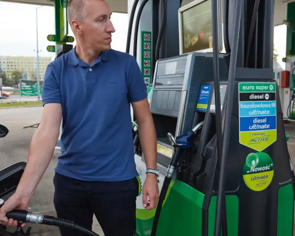 Mężczyzna dokonuje tankowania swojego samochodu na stacji paliw. W ręku trzyma pistolet do paliwa, gotowy do rozpoczęcia procesu.