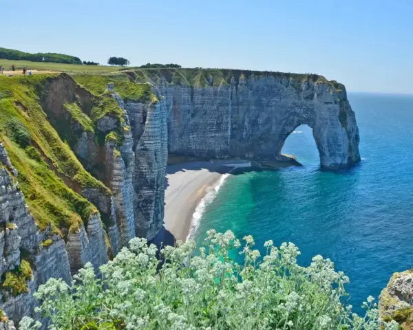 Falaises d'Étretat, France. L'arche naturelle de la Porte d'Aval se dresse fièrement au-dessus de la plage de galets. Le **gr 21** serpente le long de la côte verdoyante.