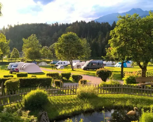 Idyllischer Campingplatz in den Dolomiten mit Wohnmobilen, Zelten und einem Teich.