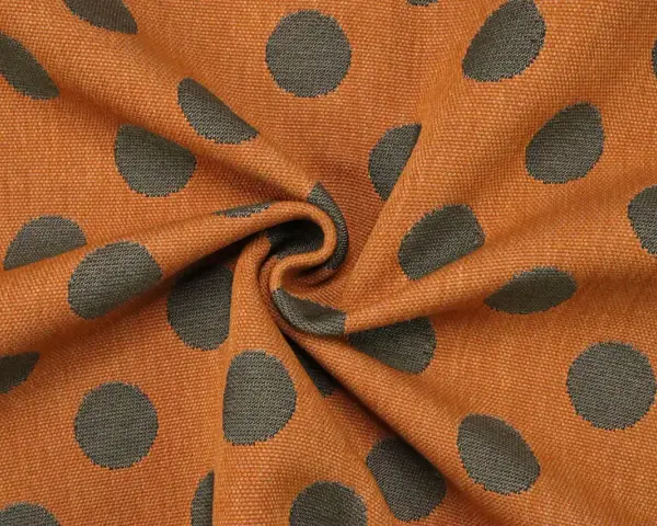 Orangefarbener Stoff mit dunklen Punkten, die wie kleine Kreise aussehen. Das Muster ist unregelmäßig und wirkt lebendig.