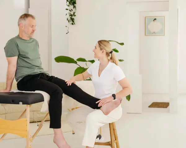 Physiotherapeutin hilft Mann mit Ischias-Schmerzen bei Dehnübungen. Sie streckt sein Bein, um die Nerven zu entlasten.