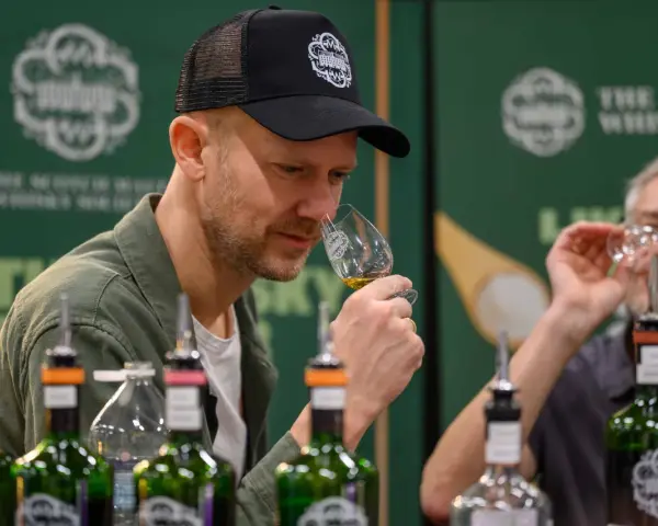 Mann mit Kappe riecht an einem Whiskyglas bei einer Whisky Messe. Flaschen stehen auf dem Tisch.