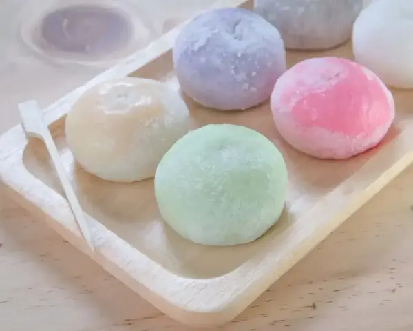 Kolorowe mochi na drewnianej tacce. Chcesz wiedzieć, jak zrobić mochi? Te słodkie kuleczki wyglądają pysznie!