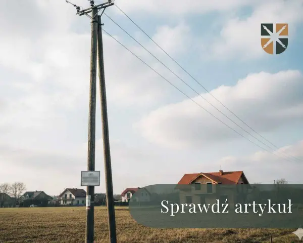 Drewniany słup z przewodami tworzy linię napowietrzną nad polami i domami.