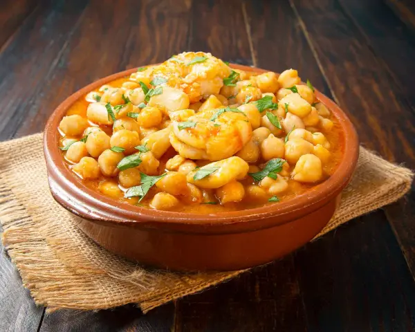 Un plato de barro con garbanzos y langostinos, adornado con perejil fresco, sobre una mesa de madera rústica.