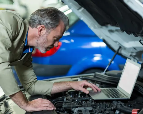 Mechanik z laptopem przy otwartej masce samochodu.
