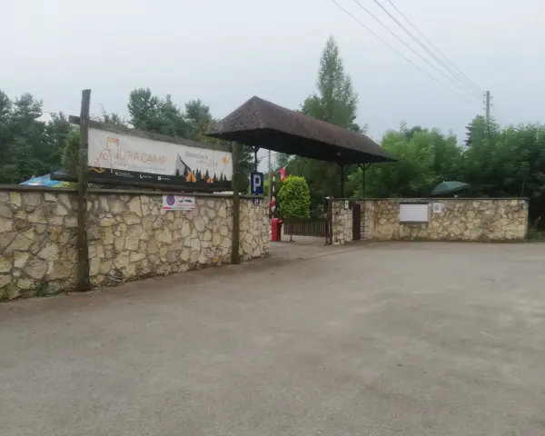 Wjazd na siamoszyce camping przez kamienny mur. Baner "Jura Camp" zaprasza do wypoczynku wśród drzew.
