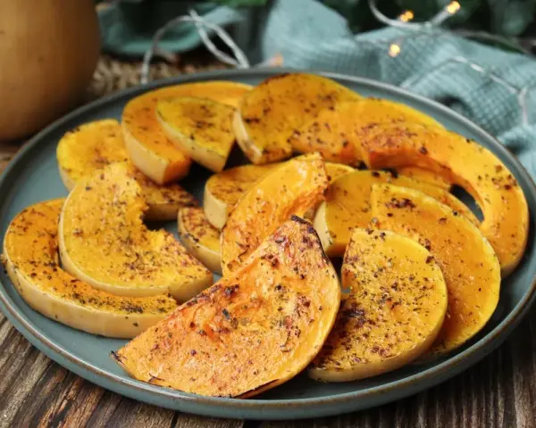 Rodajas de calabaza a la plancha, doradas y especiadas, servidas en un plato azul sobre una mesa de madera.