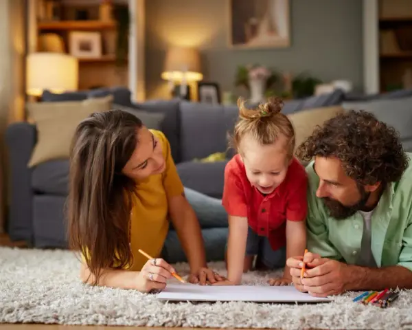 Rodzina rysuje na dywanie. Mama, tata i dziecko cieszą się wspólnym czasem, planując, ile jest zwrotu z podatku za dziecko.