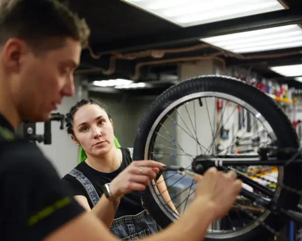 Mechanik rowerowy wyjaśnia, ile kosztuje wymiana dętki w rowerze, podczas gdy kobieta z zielonymi włosami uważnie słucha.