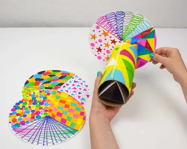 Manos creando manualidades con material reciclado para adolescentes: un caleidoscopio con tubos de cartón y discos decorados con patrones coloridos.