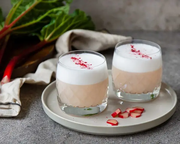 Två glas med rabarber sour, toppade med skum och strödd rabarberpulver. En härlig syrlig sommardröm.
