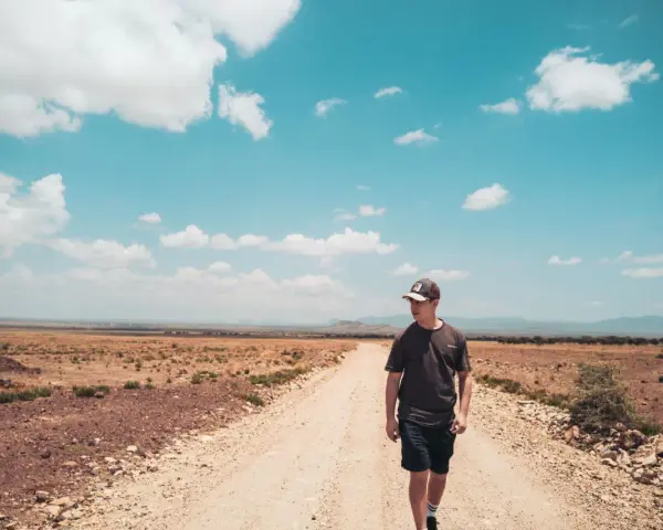 Ein junger Mann mit Kappe geht auf einer staubigen Straße in der afrikanischen Savanne. Ein bezahltes Praktikum im Ausland nach dem Abitur ist ein Abenteuer.