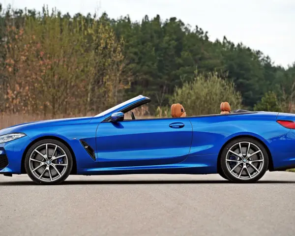 Niebieski roadster z brązową skórzaną tapicerką, zaparkowany na drodze z widokiem na las.