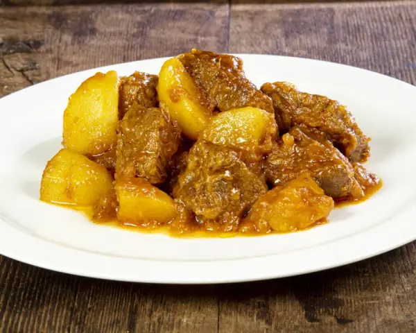 Un saporito spezzatino di vitello con patate, servito su un piatto bianco, su uno sfondo di legno scuro.