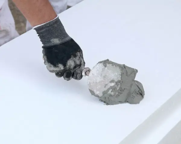 Ręka w rękawicy nakłada zaprawę na styropian. To pokazuje, jaki klej do styropianu wybrać do prac termoizolacyjnych.