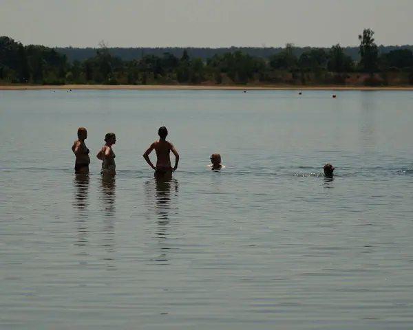 Menschen genießen das naturbad luppa an einem sonnigen Tag. Einige stehen im Wasser, andere schwimmen.