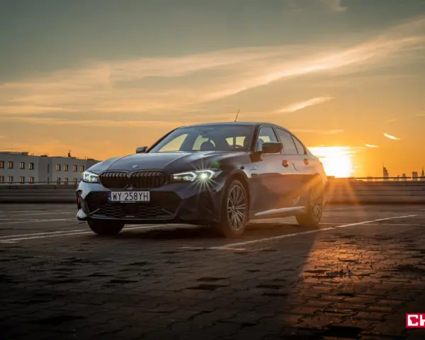 Ciemnoszara limuzyna BMW 330e na parkingu o zachodzie słońca.