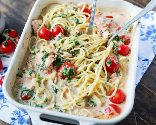 Cremige Lachs Spinat Pasta mit Kirschtomaten in einer Auflaufform, serviert mit zwei Gabeln.