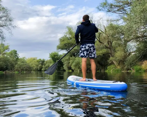 Mann auf SUP-Tour auf einem ruhigen Fluss, umgeben von üppiger Vegetation.
