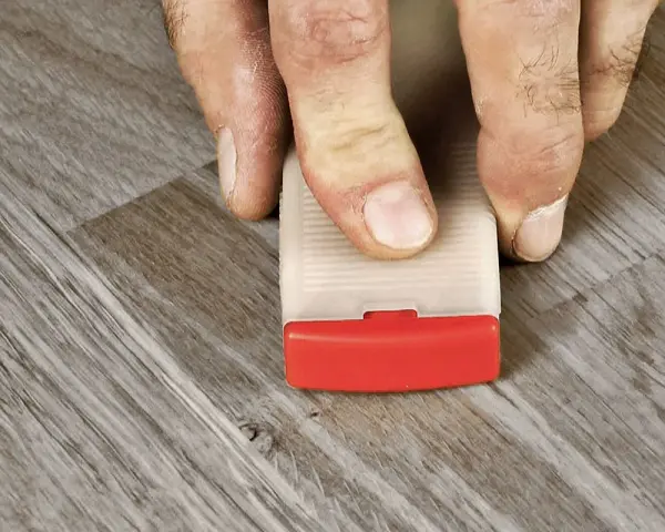 Fingrar använder en kil för att laga laminatgolv.