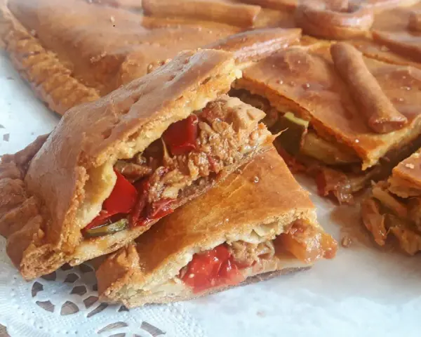 Una deliciosa empanada de carne, cortada en porciones, revela su jugoso relleno de carne deshebrada y pimientos rojos.