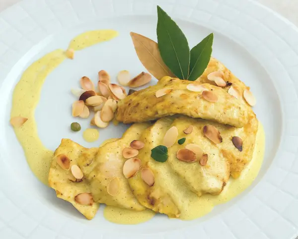Délicieux poulet au curry, garni d'amandes effilées et d'une sauce onctueuse, servi sur une assiette blanche.