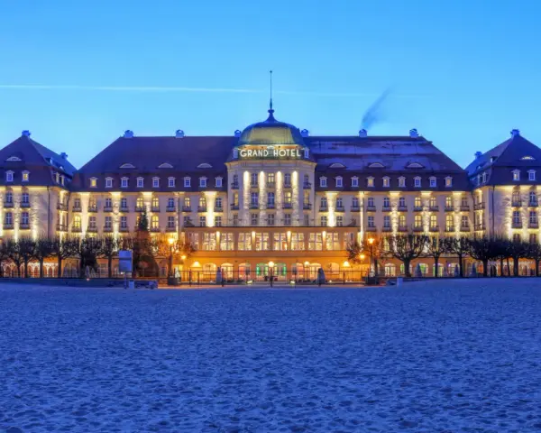 Elegancki Grand Hotel, część sieci luksusowych hoteli, lśni nocą na tle plaży.
